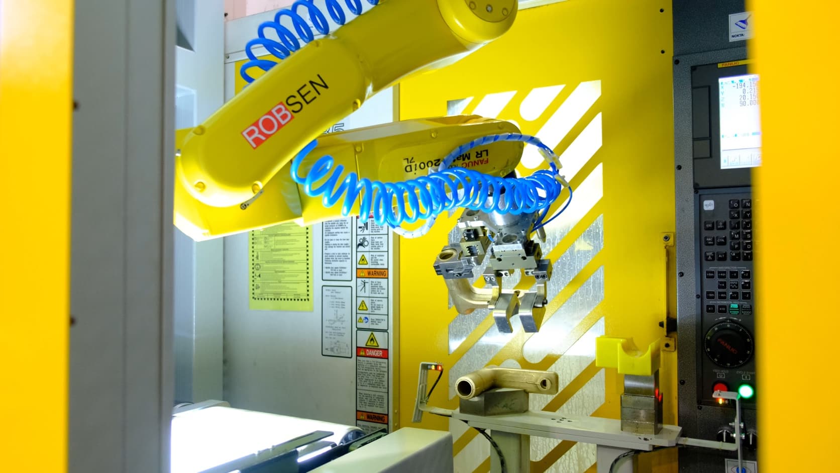 Robsen-branded robot with a dual-gripper tool holding a brass workpiece beside a CNC machine.