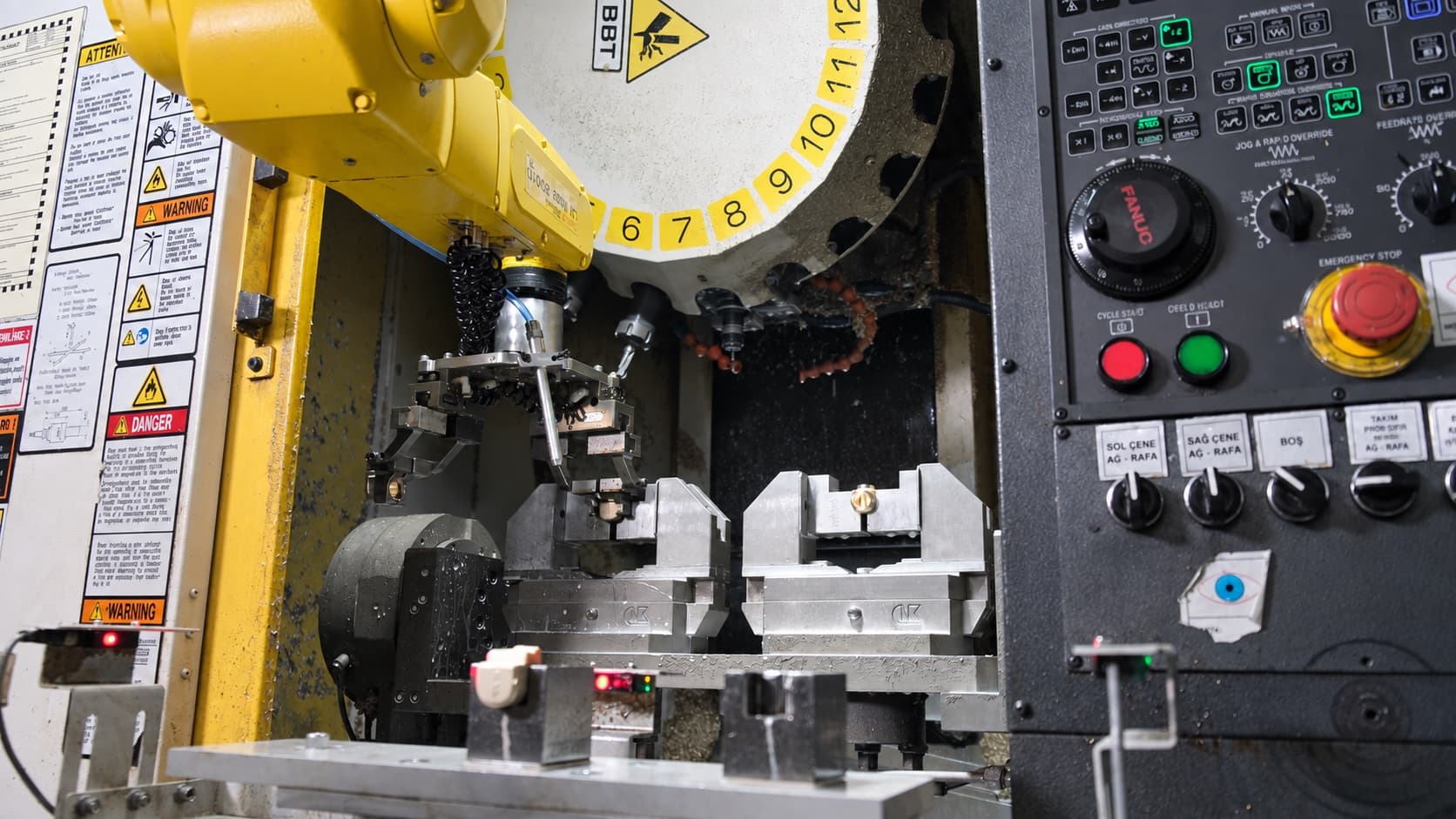 Close-up of a FANUC robot positioning a workpiece above two automatic CNC fixtures.