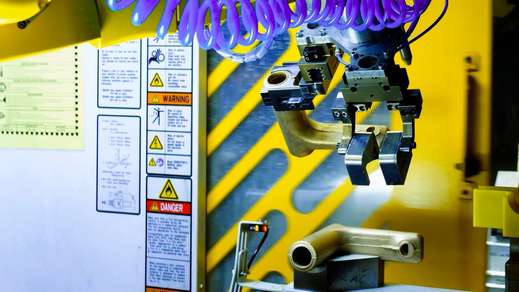 Close-up of a dual-gripper tool with a brass workpiece in one gripper and the other gripper open.