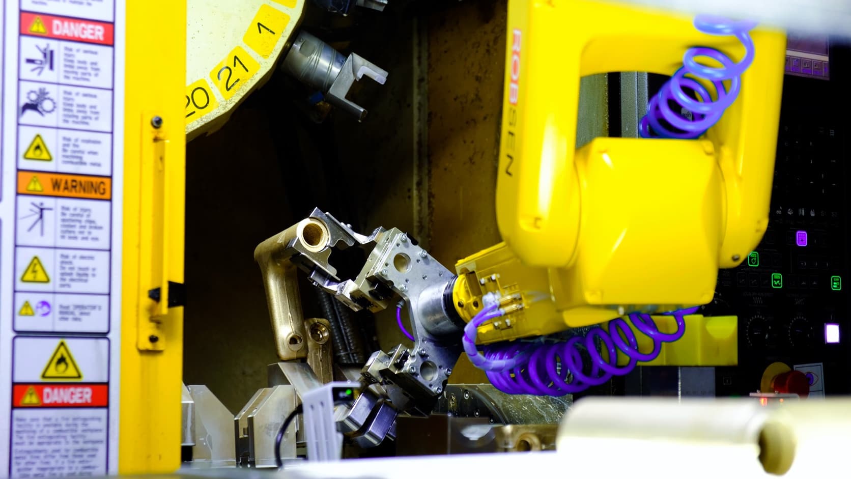 Yellow industrial robot with a dual-gripper assembly handling a brass workpiece inside a CNC machine.
