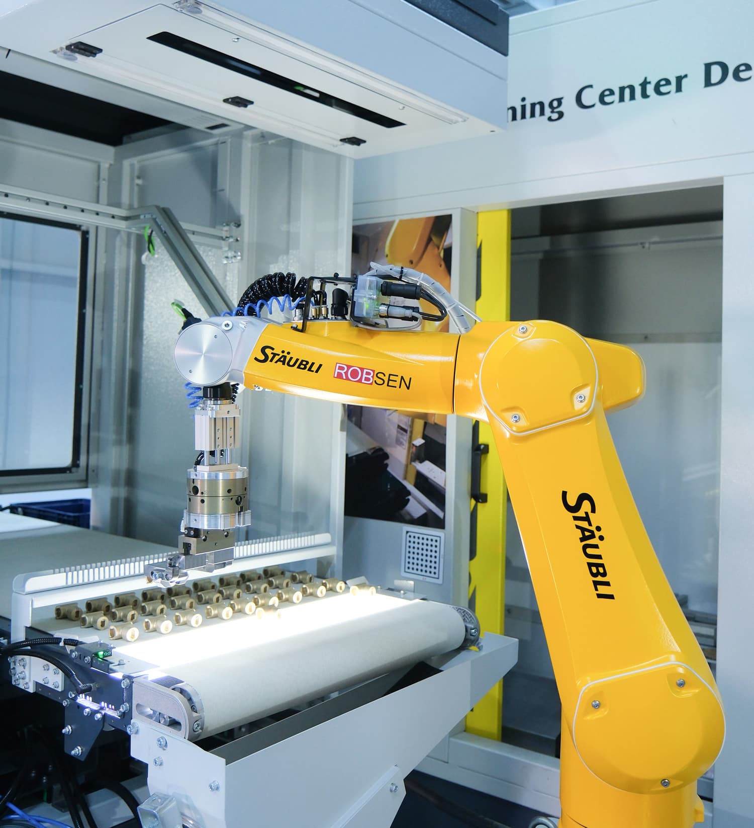 Close-up of a yellow Stäubli robot and separated forged components on the conveyor inside an IROCUBE MS60L transfer-machine tending cell.